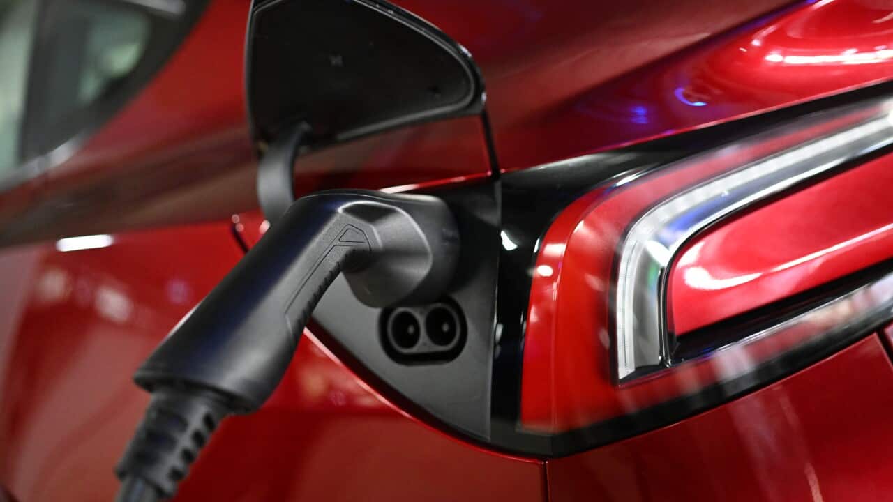 A black charger handle connected to a charge port on a red electric car.