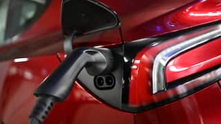 A black charger handle connected to a charge port on a red electric car.