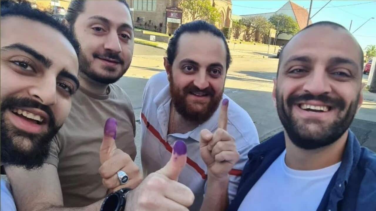 Four men are smiling raising their thumbs that are inked with purple.