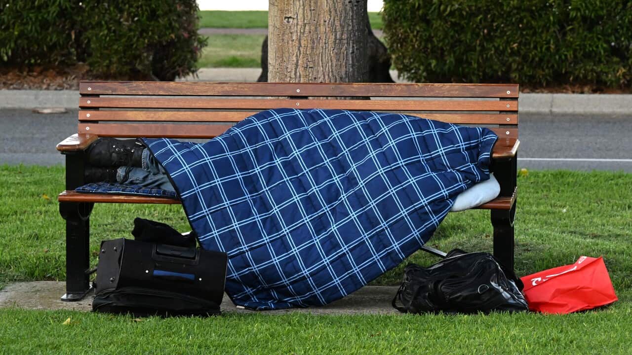 Homeless person lying under a rug on a bench.