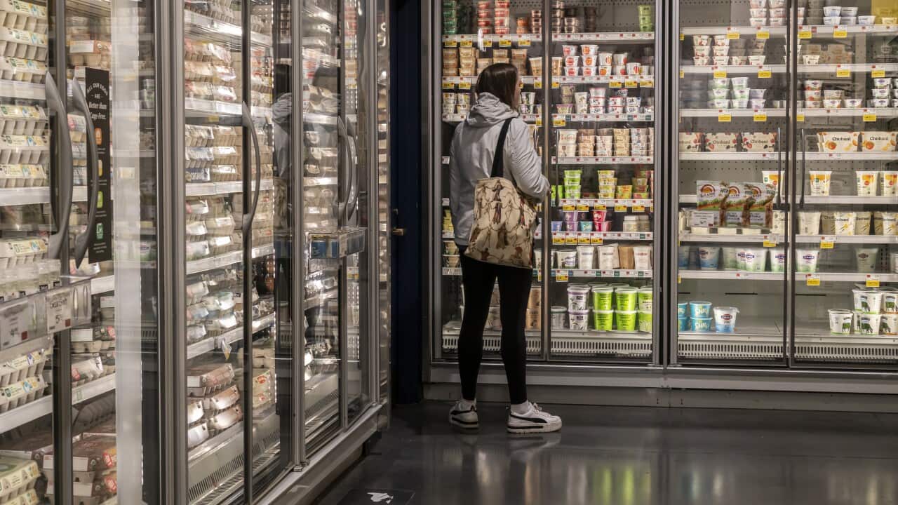 A woman is staring at a fridge aisle at a supermarket.