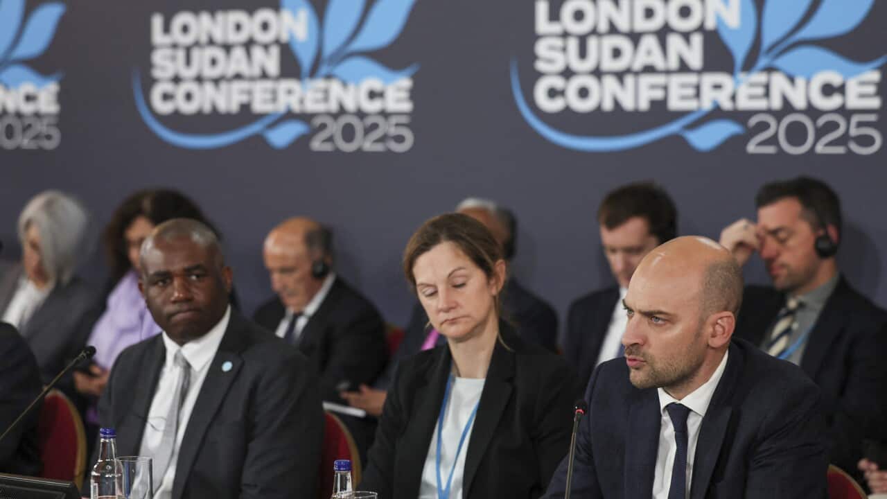 Two men and a woman sit at a table with microphones in front of them