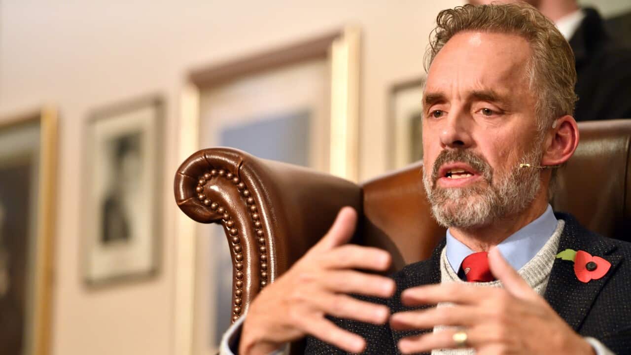 A man with grey hair talks in an arm chair.