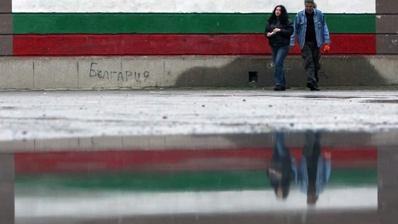Bulgarians walk past a Bulgarian national flag