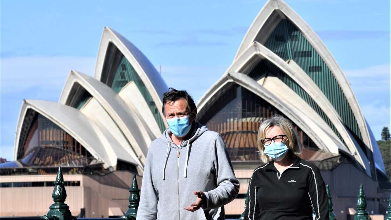 Members of the public, wearing masks, walk past the Sydney Opera House in Sydney.