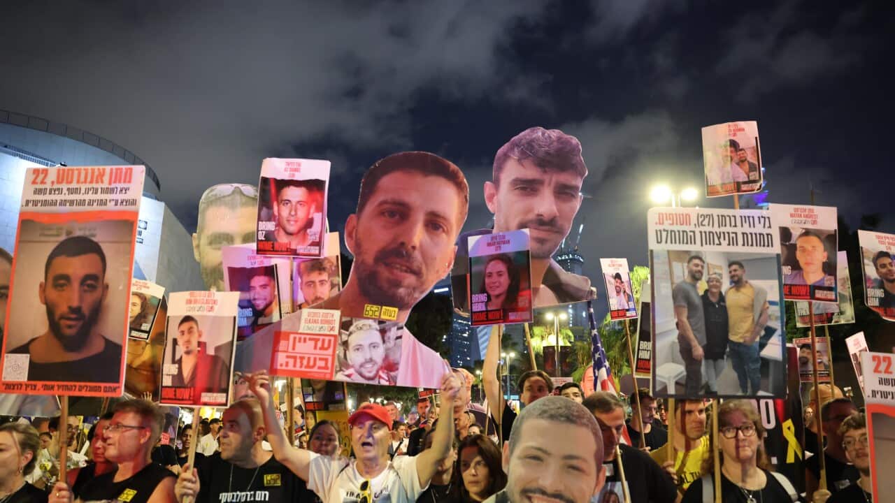 A group of protesters hold up placards with images of people's faces and Hebrew writing.