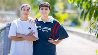 Two young female soccer players stand together and smile at the camera.