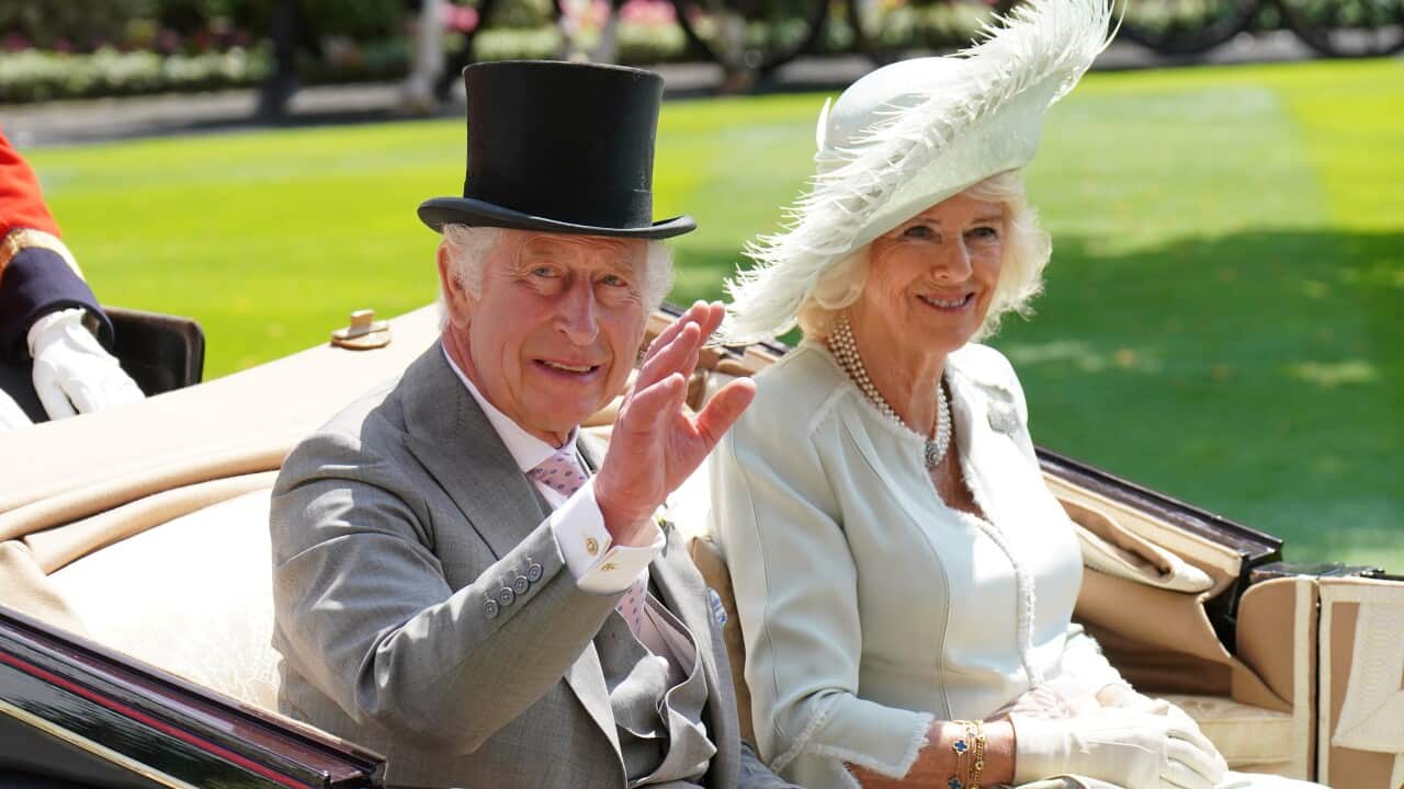 King Charles and Camilla dressed in very formal attire and hats, while sitting in a carriage and waving