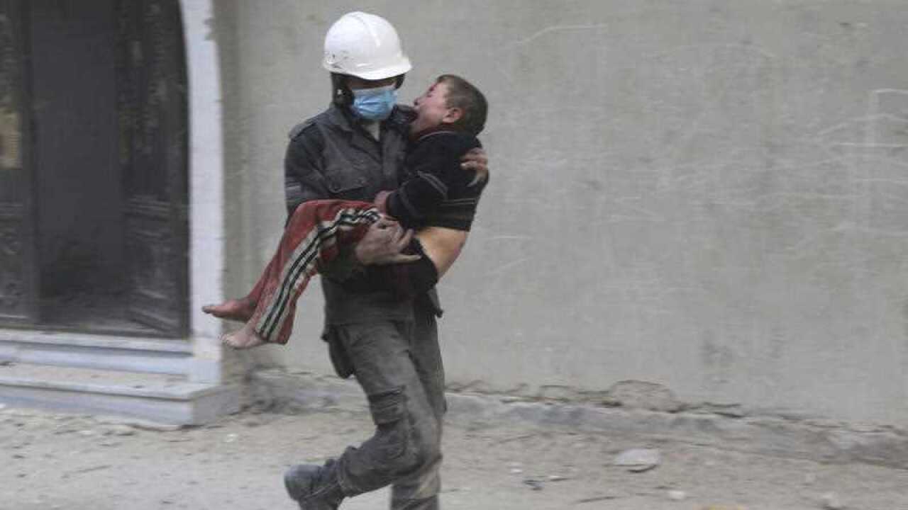 In this photo provided by the Syrian Civil Defense group known as the White Helmets, shows a member of the Syrian Civil Defense group carries a boy who was wounded during airstrikes and shelling by Syrian government forces in Ghouta, Syria.