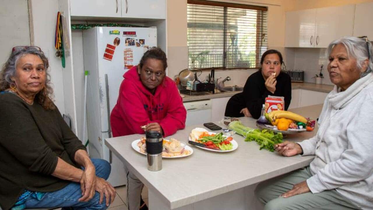 Four people sit and stand around a kitchen bench with healthy food displayed
