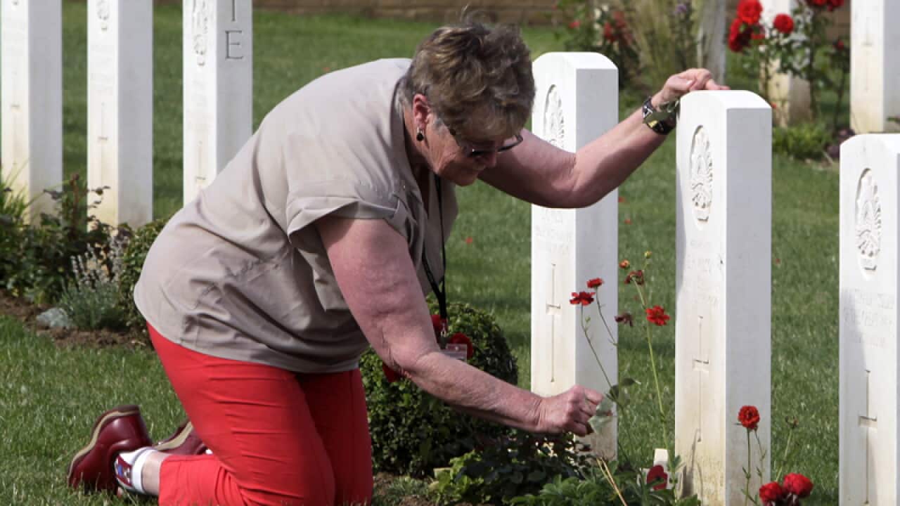 A woman lays a flower on a grave at Fromelles, France
