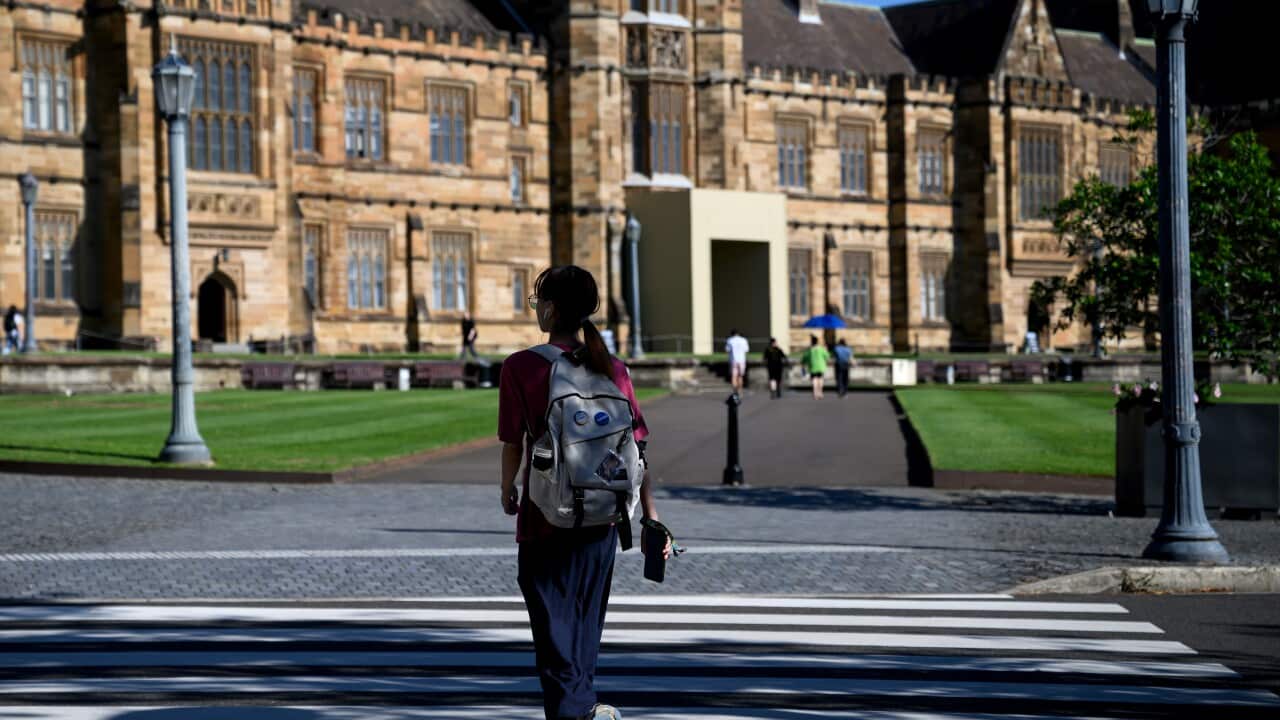 A young woman wearing a backpack walks towards a sandstone building.