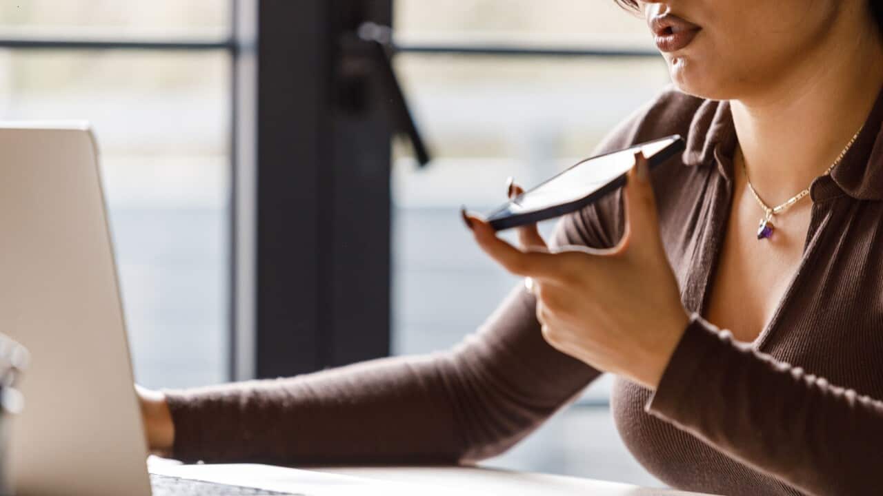 Young woman using laptop and talking on the phone via speakerphone
