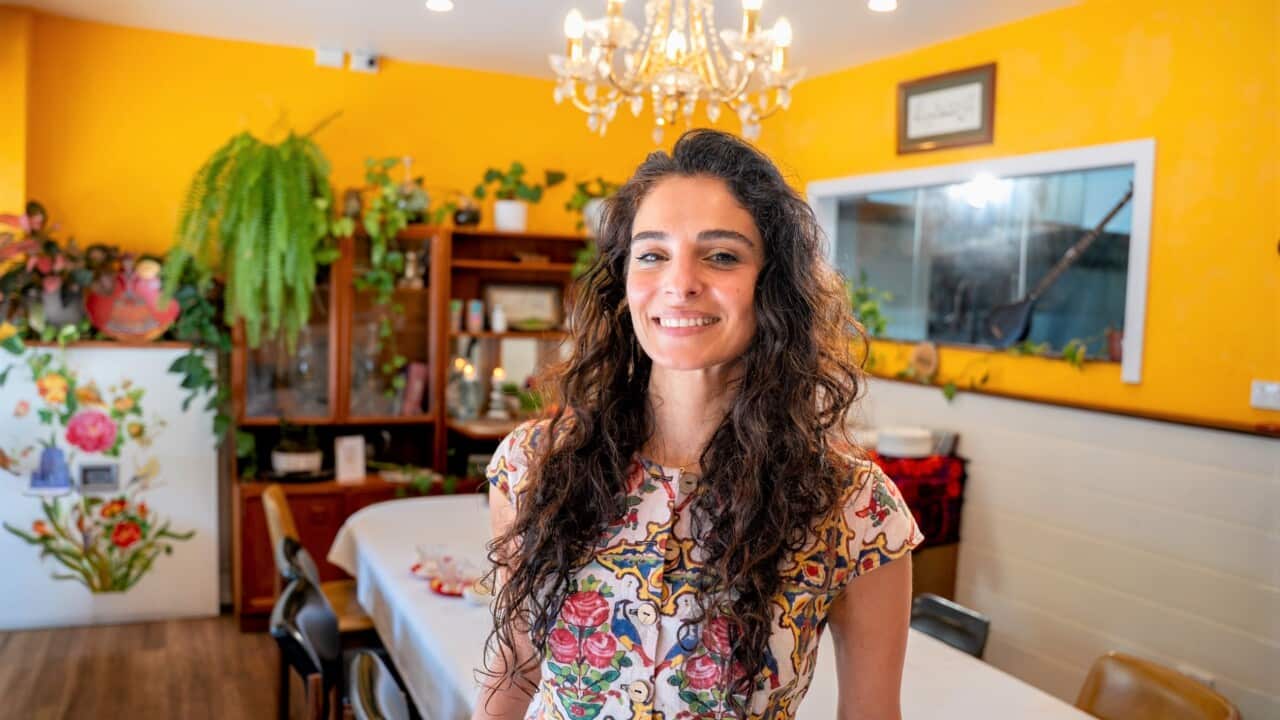 A woman with long brown hair and wearing a floral dress stands in an empty restaurant dining room