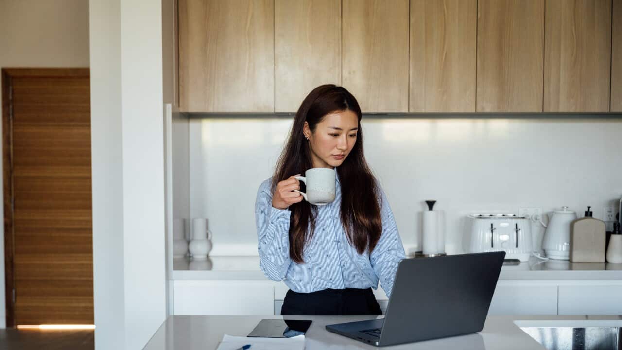Young Asian businesswoman smiling while using laptop in a bright modern kitchen