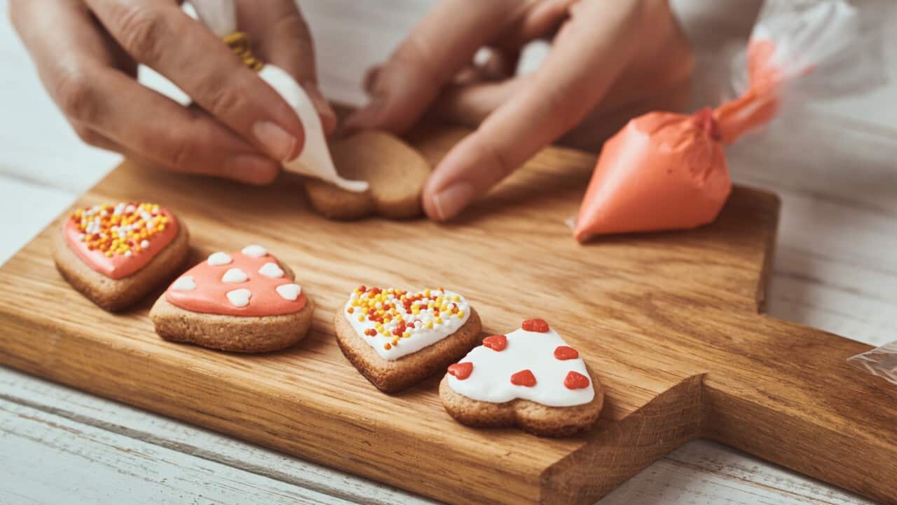 Decorating gingerbread cookies with icing. Woman hand decorate cookies in shape of heart, closeup