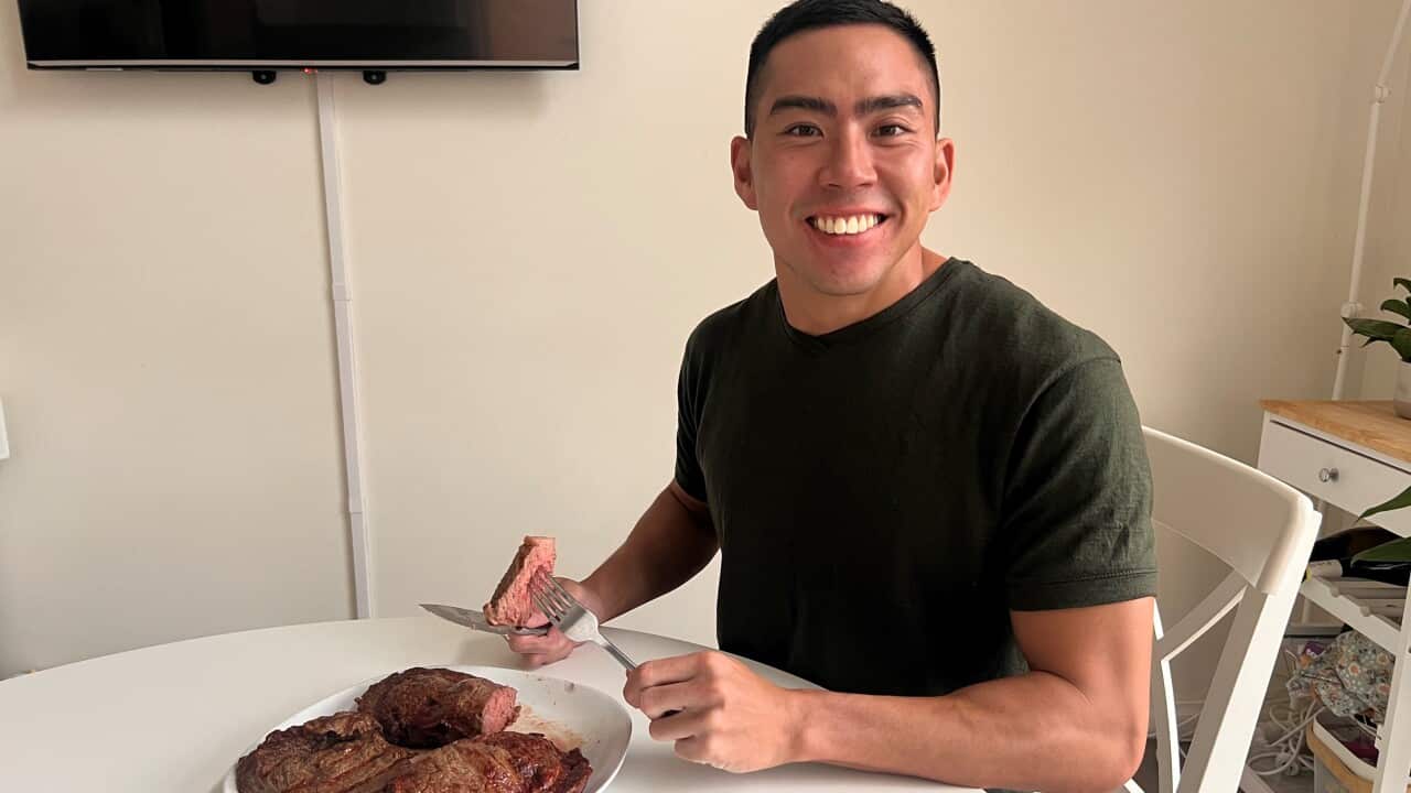 A young man in a black t-shirt smiles with two large cooked steaks with nothing else on his plate