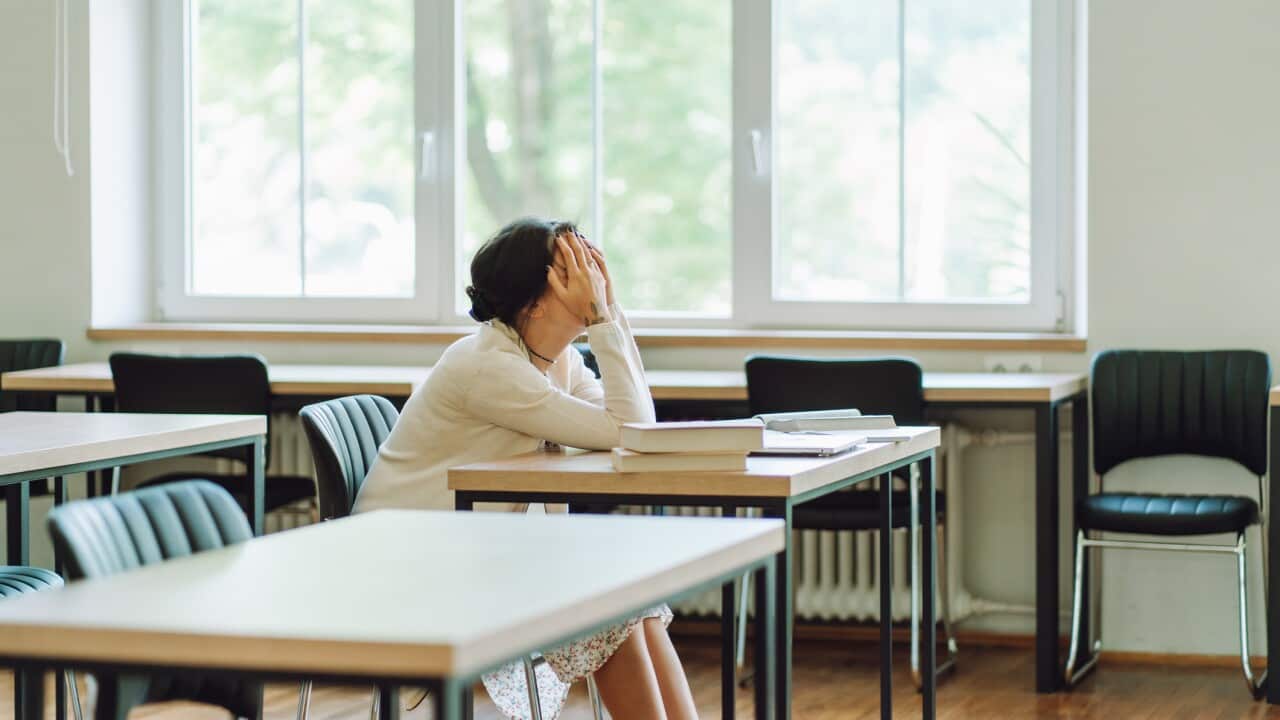 Exam failure: sad woman with her face in her hands sits at desk.