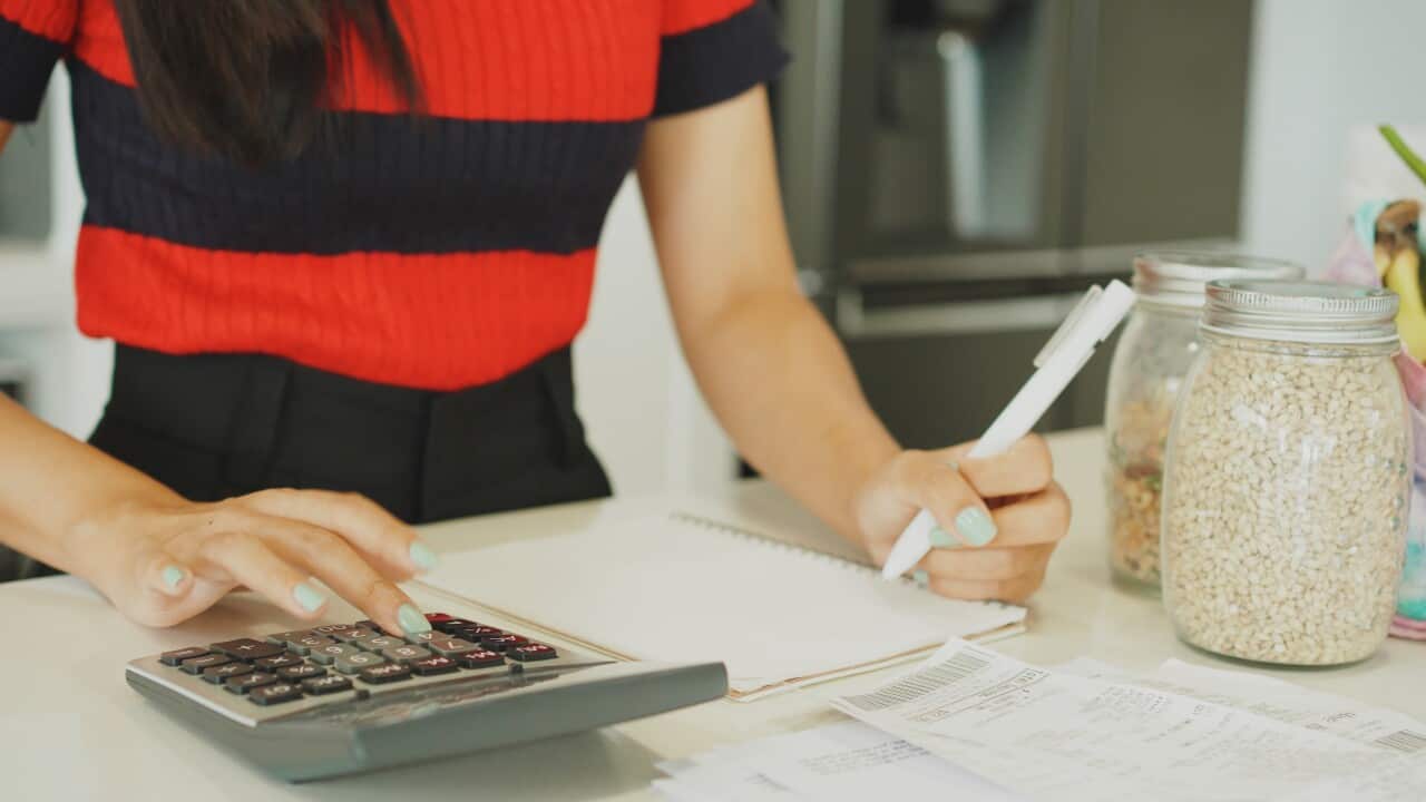 Young woman typing into a calculator in a kitchen.