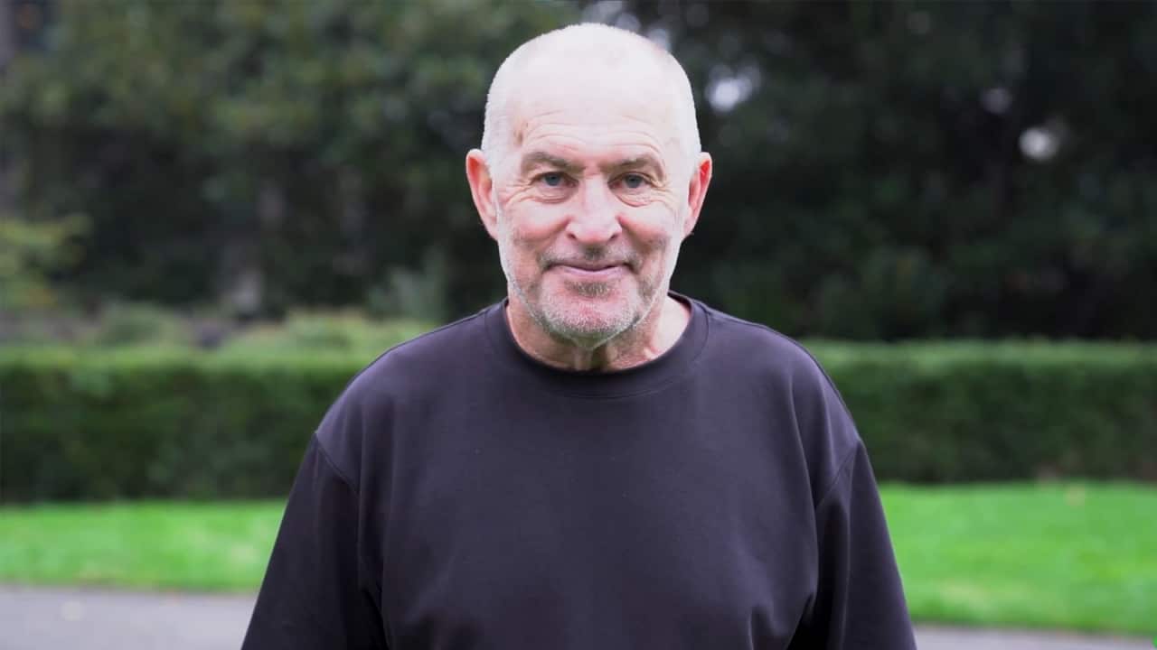 A man wearing a black T-shirt smiles into the camera.