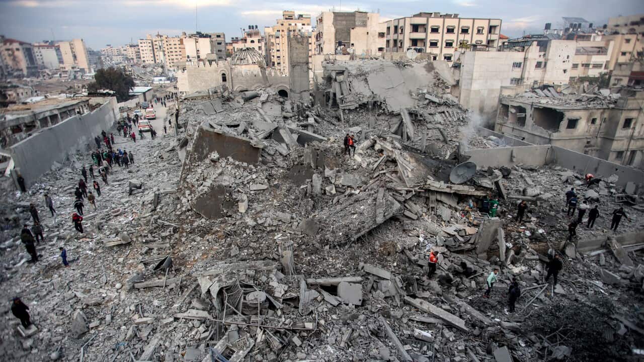 People and first responders inspect the rubble of a collapsed residential building.