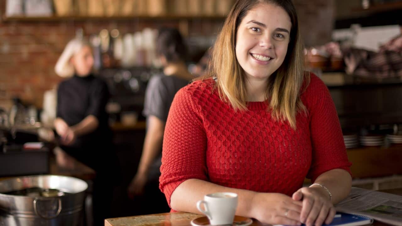 Una mujer con un top rojo de punto se sienta en un café y sonríe.