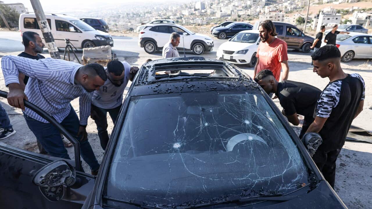 A group of men inspect a car that has been damaged in an air strike.