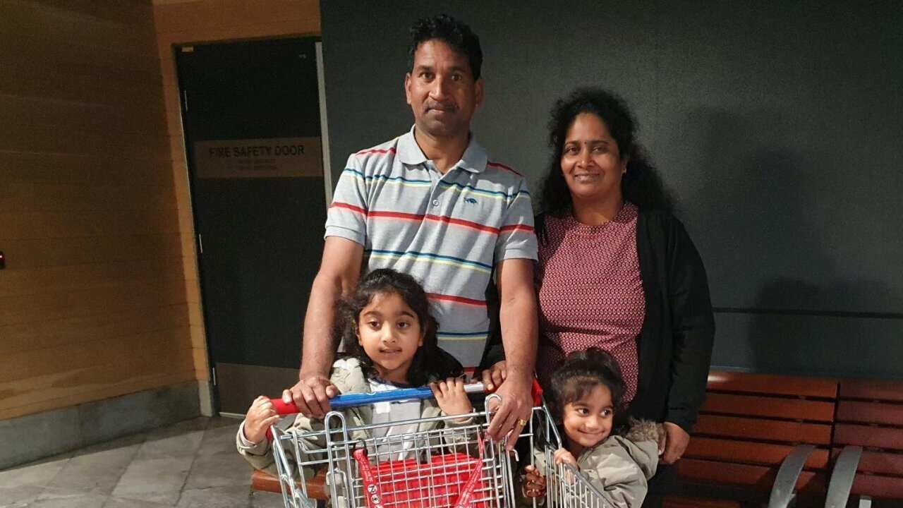 A man and a woman standing with two girls standing in front of them. There is a shopping trolley in front of them.
