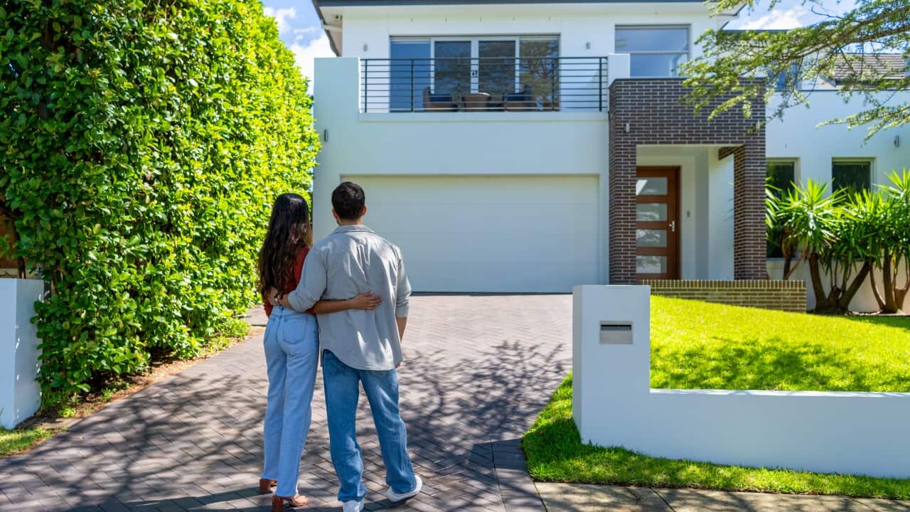 Una pareja está de espaldas a la cámara frente a una casa.