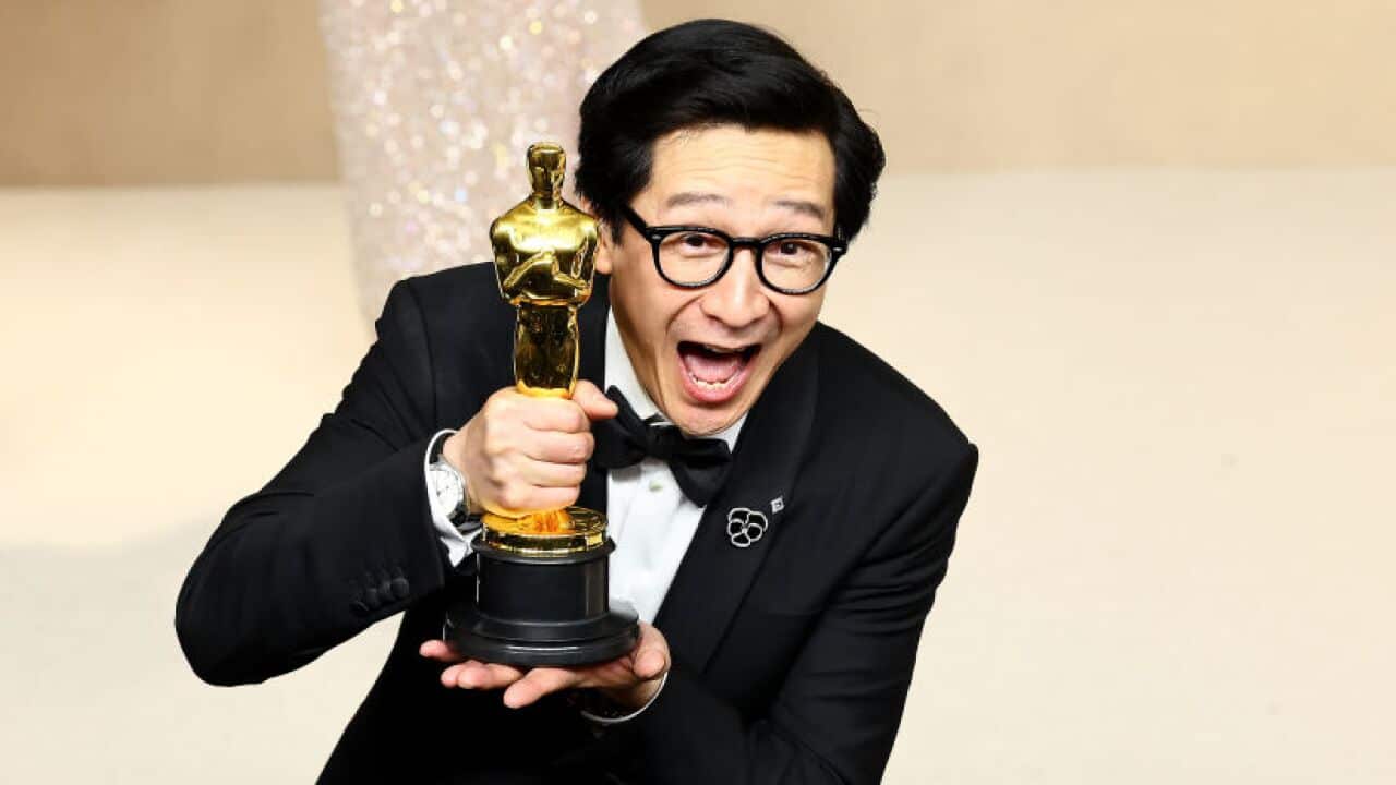 Ke Huy Quan ecstatically smiling while clutching his gold statuette after his Oscar win.