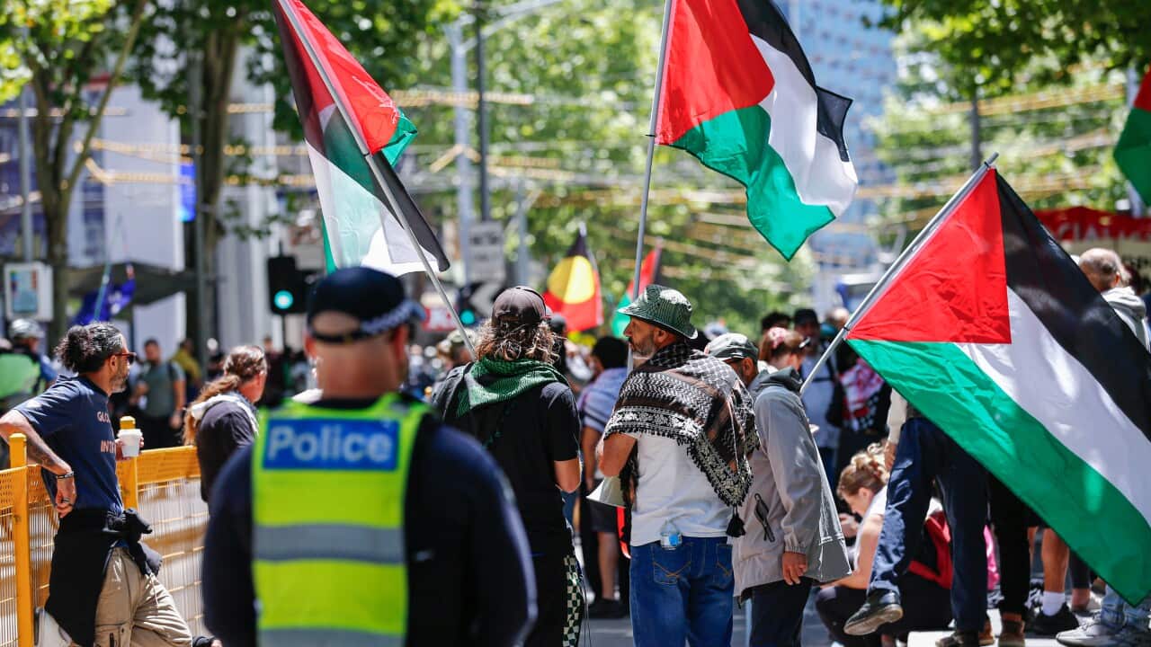 Protesters waving Palestine flags during a demonstration on a city street, a police officer watches on in the foreground.