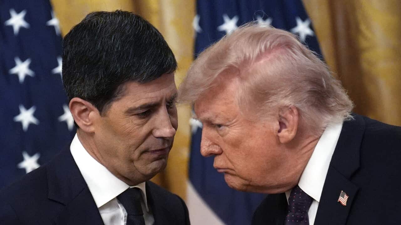 A man wearing a suit and a tie leans in to listen to another man wearing a suit and a tie