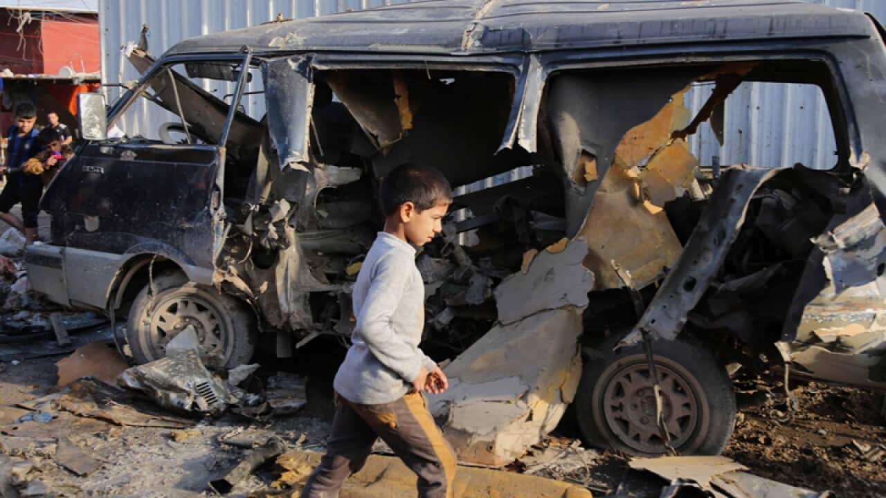 An Iraqi boy walks past a vehicle at the site of a car bomb attack.