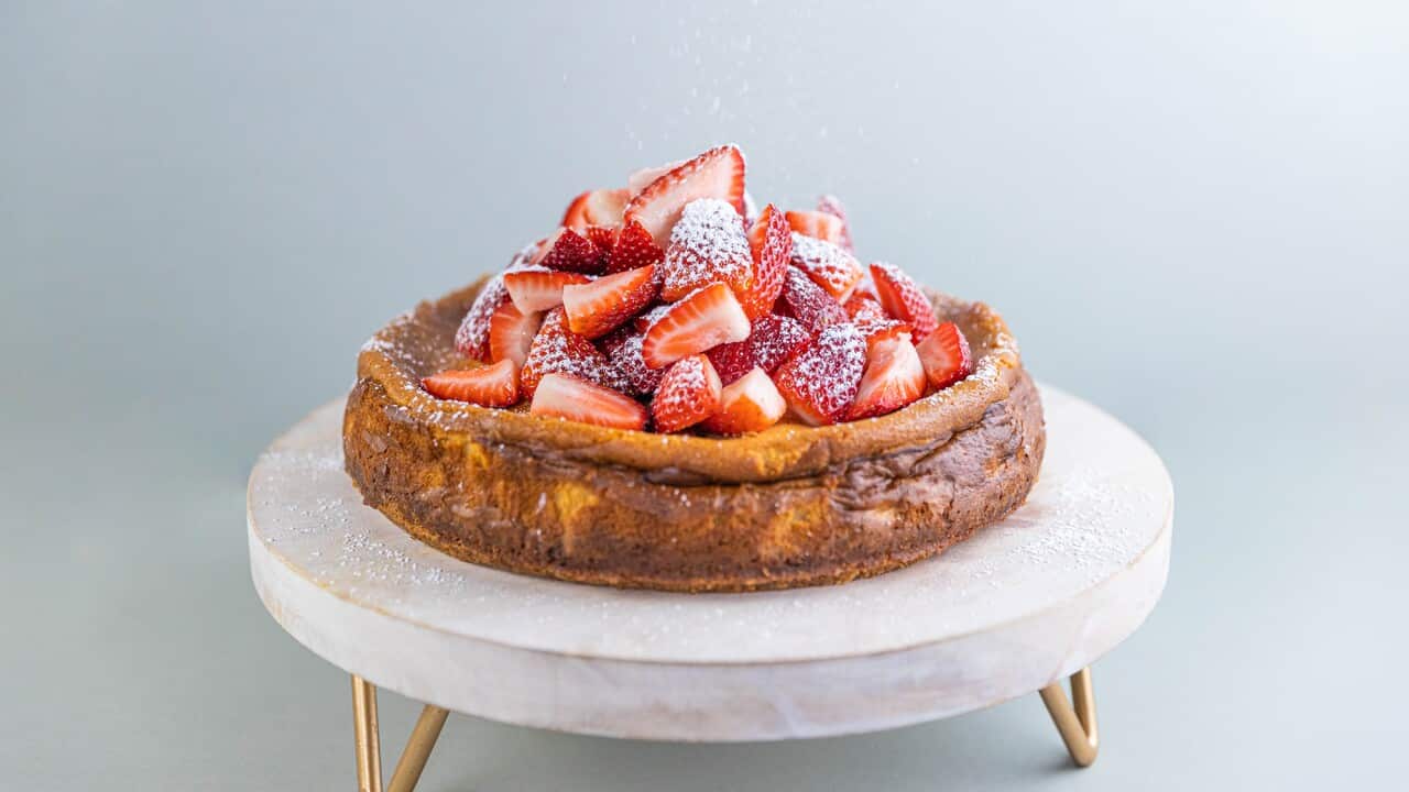 A baked cheesecake, topped with strawberries, sits on a low cake stand.