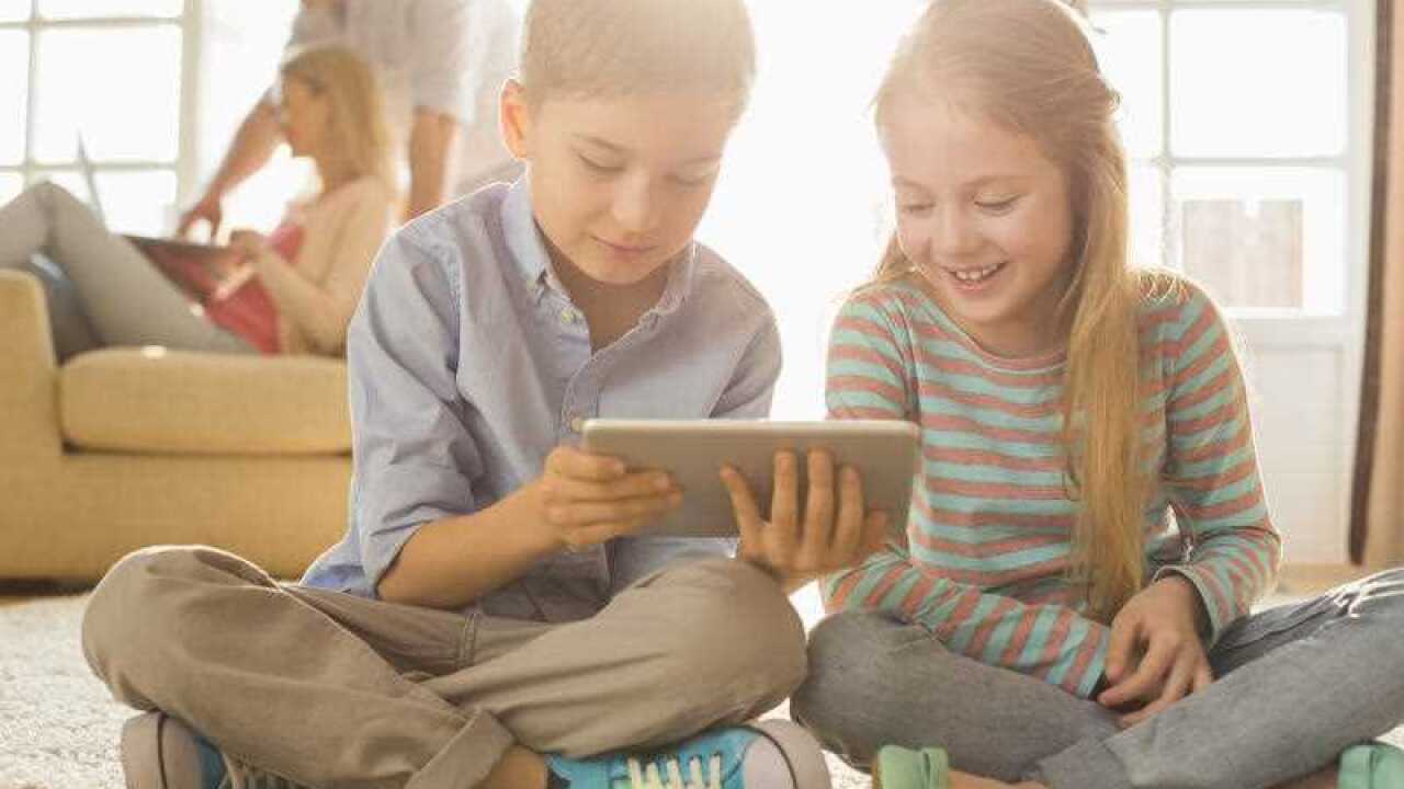 Happy siblings using digital tablet on floor with parents in background