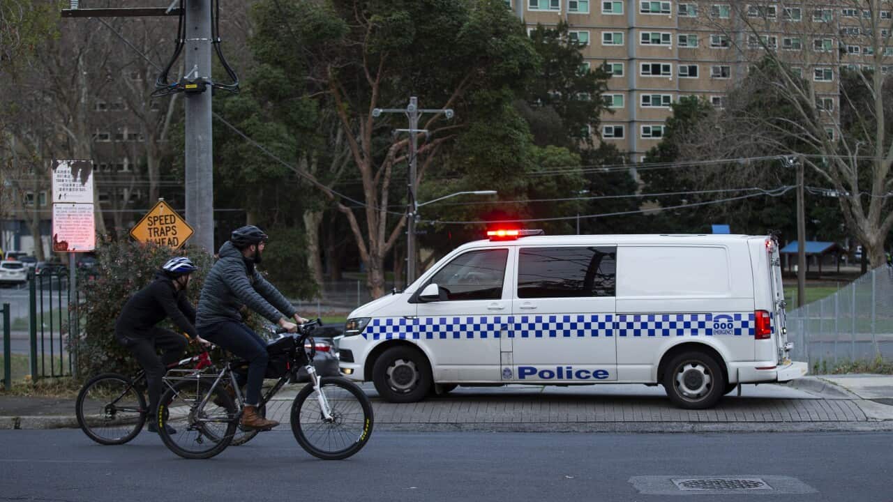 People ride past police patrols outside public housing towers on Racecourse Road in Flemington, Melbourne, Sunday, 5 July, 2020.