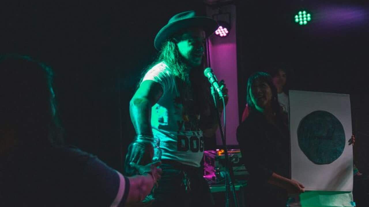 Nathan Leitch at a Barpirdhila live show presenting a raffle prize donated by Quandamook artist, Megan Cope (pictured)