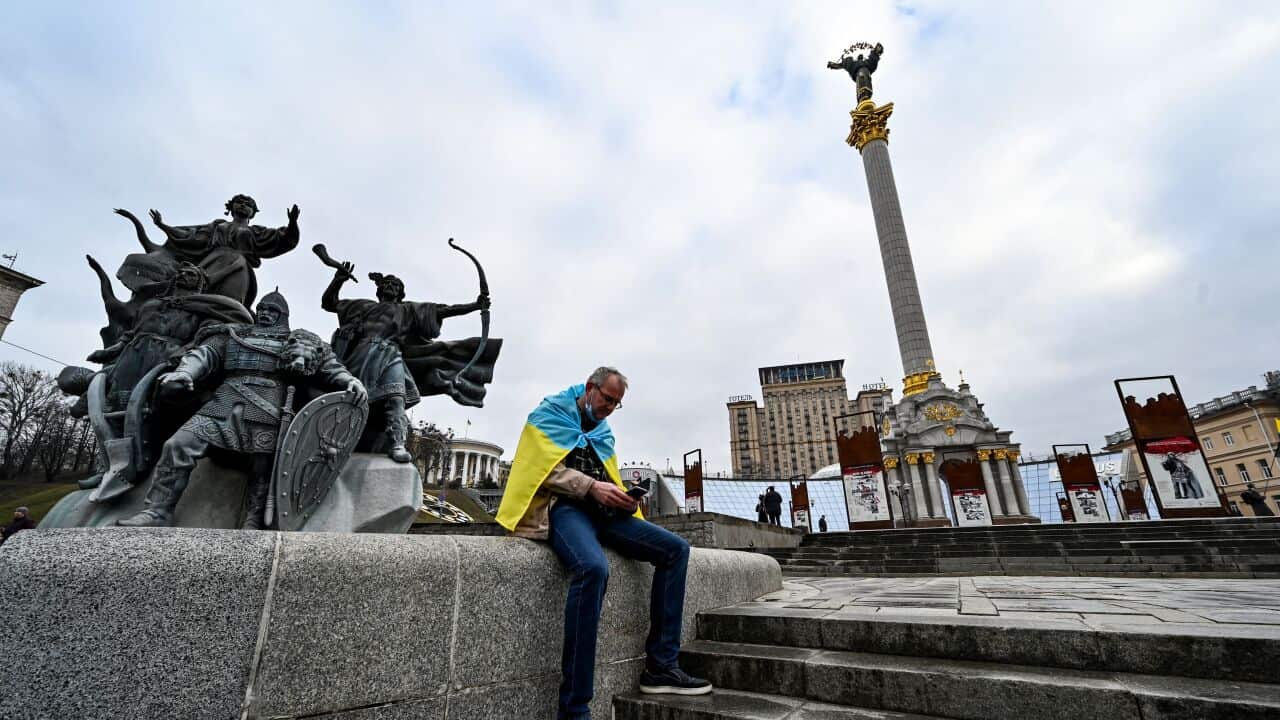 A man wrapped with an Ukrainian national flag watches news on his mobile phone as he sits at Maidan Independence Square