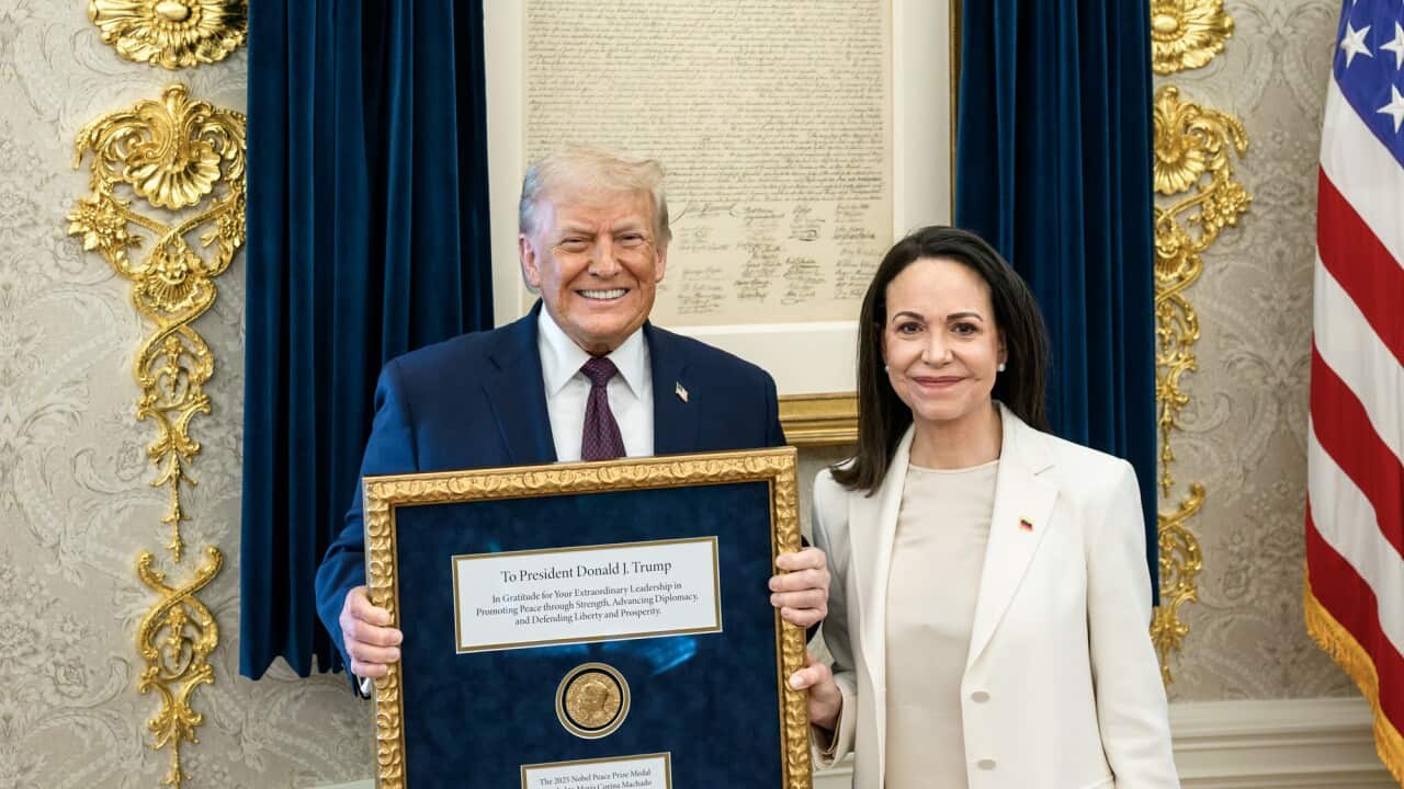 Trump and Machado pose for a photo in the gold-trimmed Oval Office. Machado is wearing a cream pantsuit and Trump is in a navy suit, carrying a framed medal.