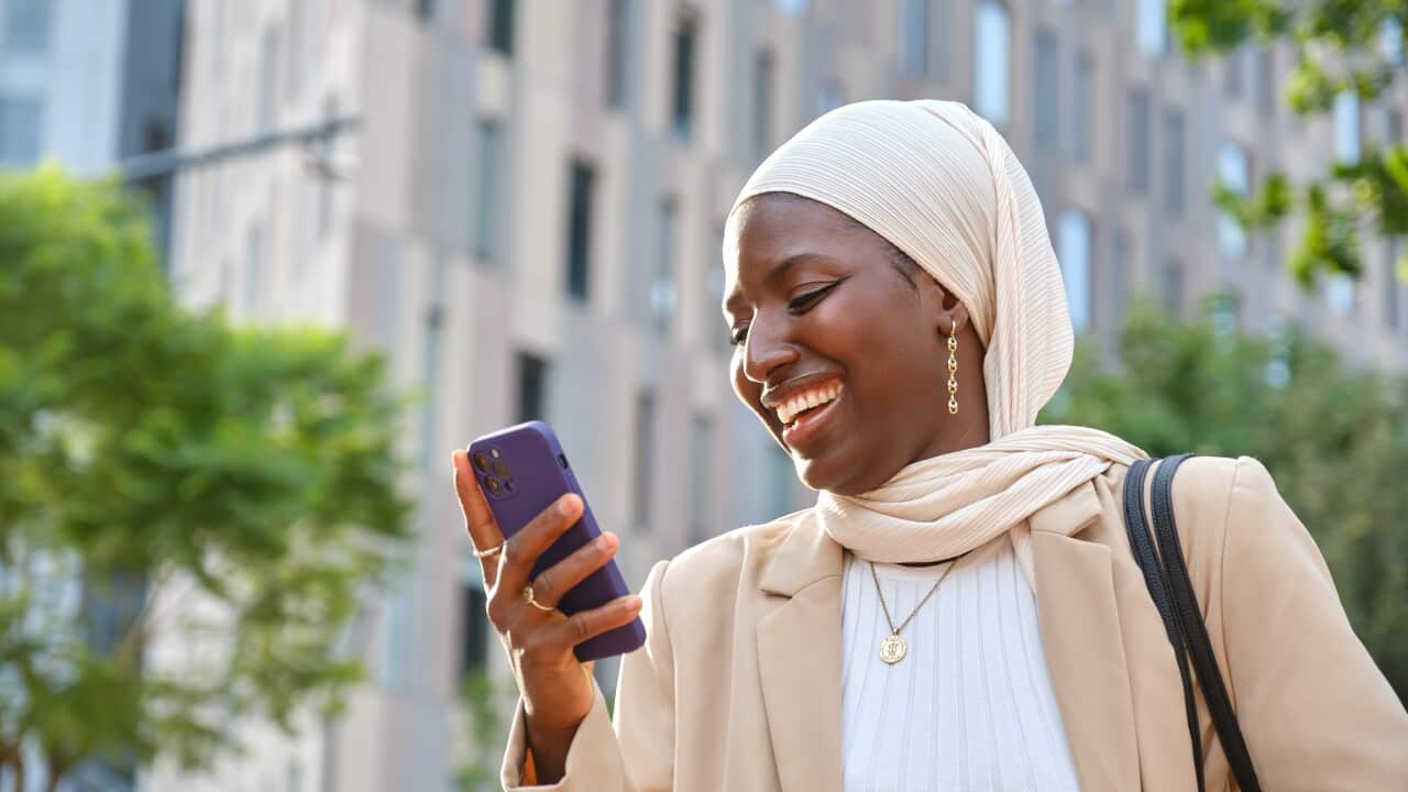 Cheerful african muslim businesswoman using phone and smiling outdoors