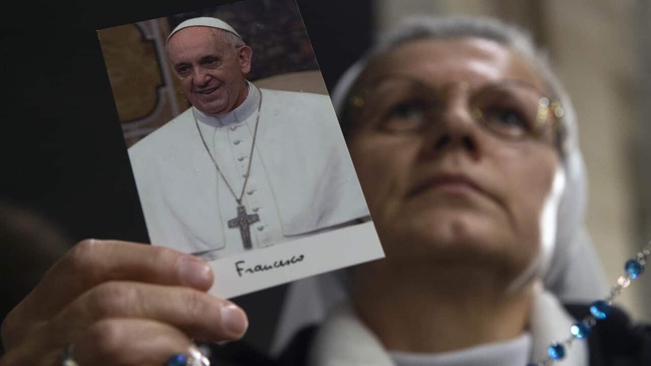 A woman with rosary beads holds up a photo of Pope Francis in white robes.