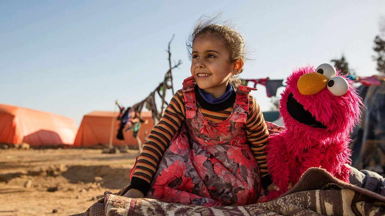 A young girl engages with Sesame Street caricature Elmo at an informal tented settlement near Mafraq, Jordan. 