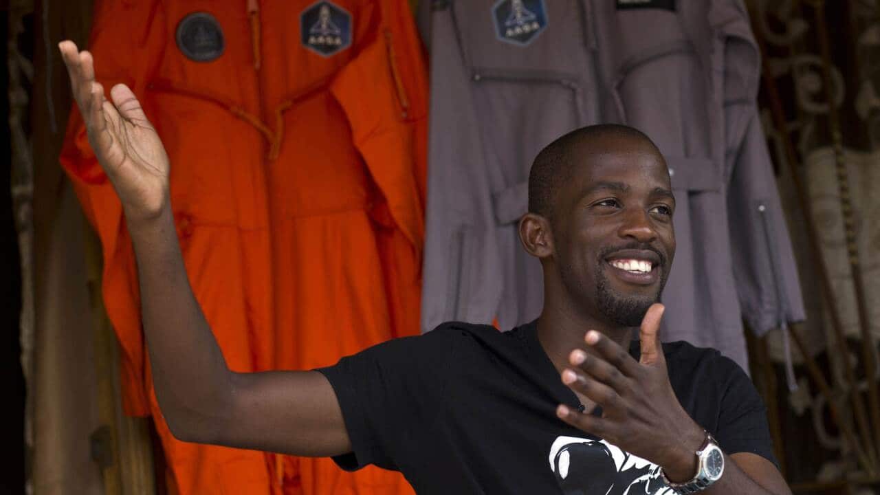Mandla Maseko speaks to a journalist in front of two NASA spacesuits - AAP-1.jpg