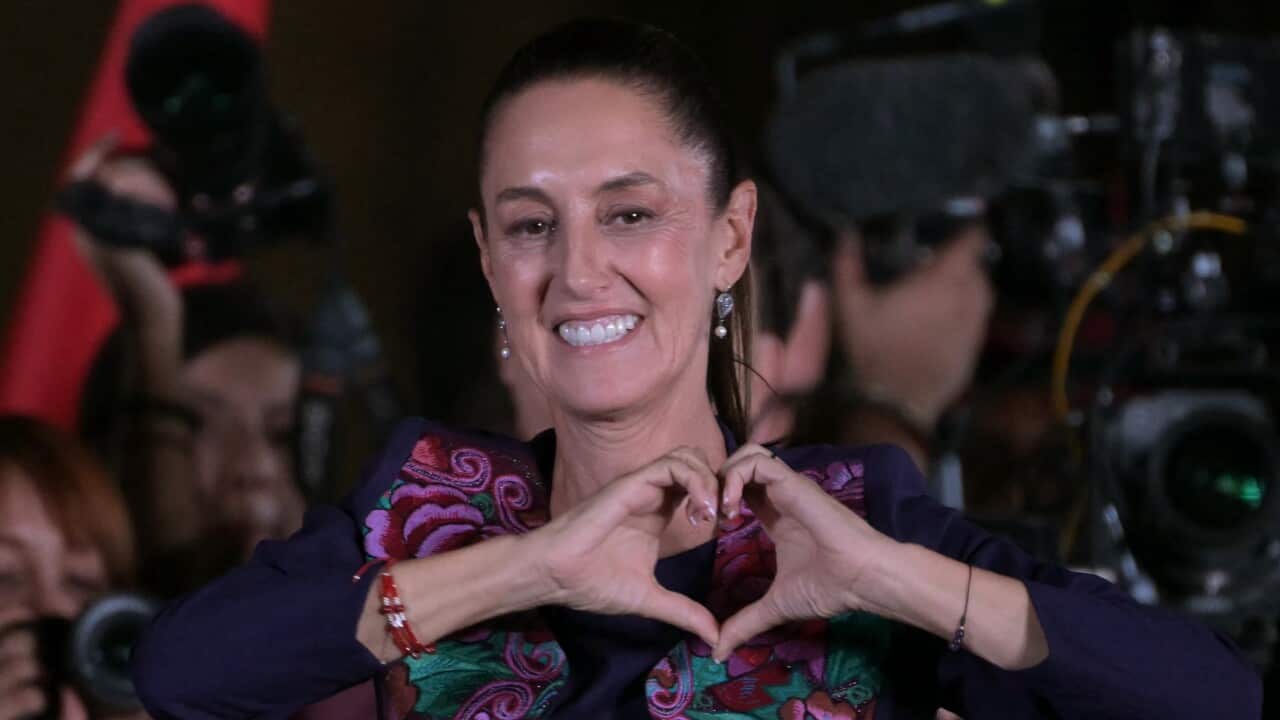 A woman makes a heart sign with her hands.