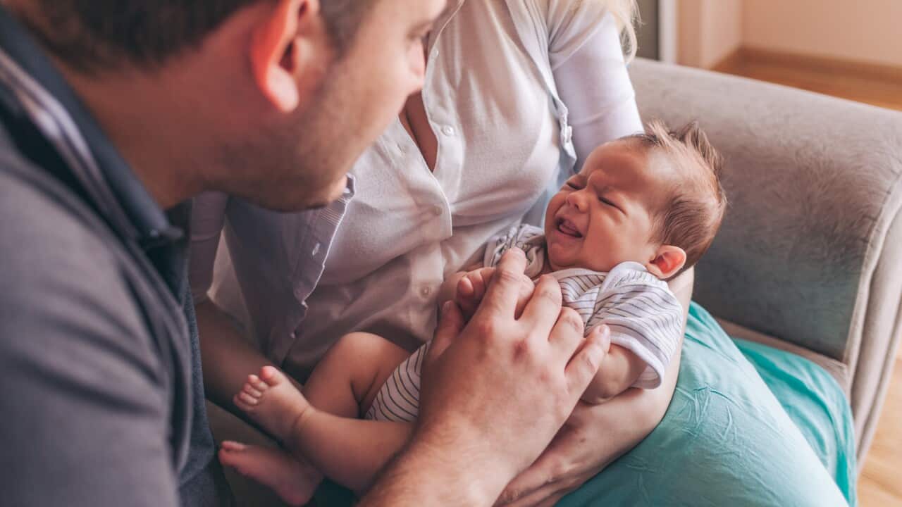 A couple holds a crying newborn baby.