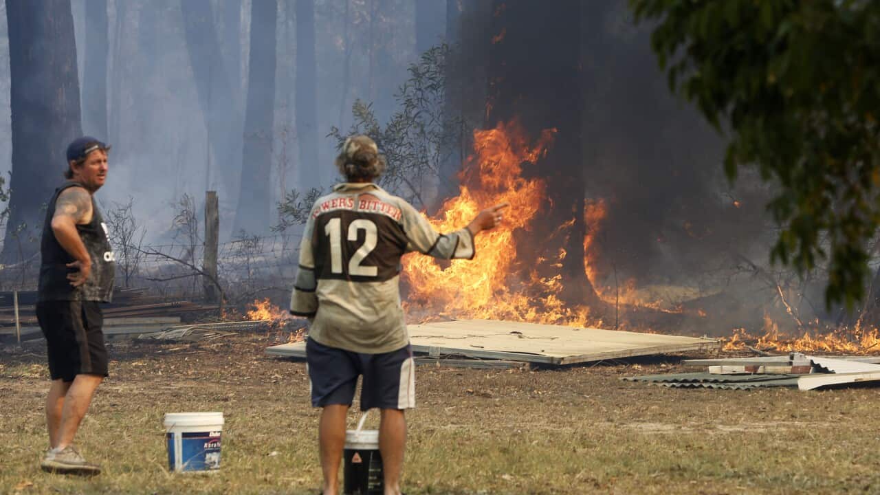 Dave Webster and Graham Rogers armed with buckets of water prepare to protect their property at Old Bar, NSW.