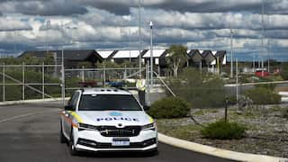 A police car sites outside a gated facility with a guard on duty.