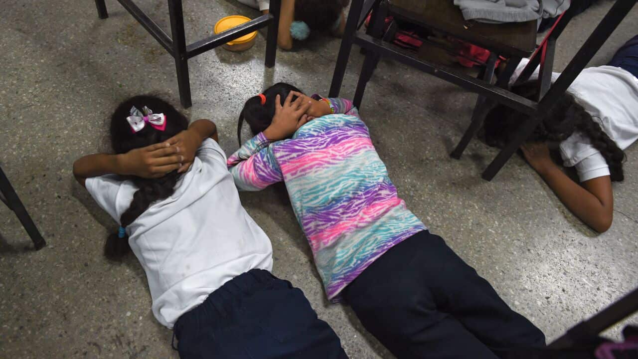 Children seen laying on the floor with their hands on their heads.