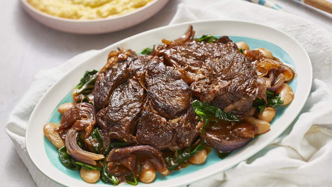 Chunky brown steaks, which look tender and moist, sit on a bed of butter beans and greens, on an oval platter.