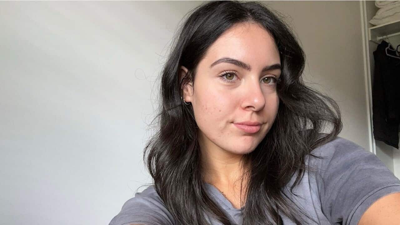 A woman with long dark hair takes a selfie with a serious expression on her face.